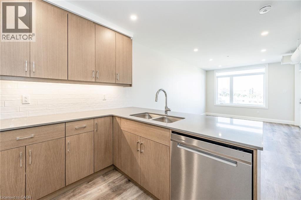 Contemporary kitchen featuring light wood-finish cabinetry, light stone countertops, a subway tile backsplash, and stainless steel appliances - 72 Erb Street E Unit# 102, Waterloo, ON - Indoor Photo Showing Kitchen With Double Sink