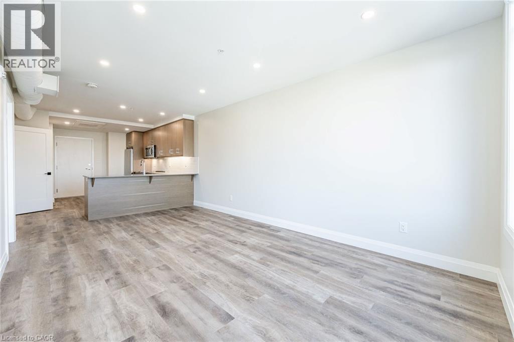 Open-concept living space featuring wood-finish flooring, recessed lighting, and a modern kitchen island with an integrated sink - 72 Erb Street E Unit# 102, Waterloo, ON - Indoor Photo Showing Kitchen