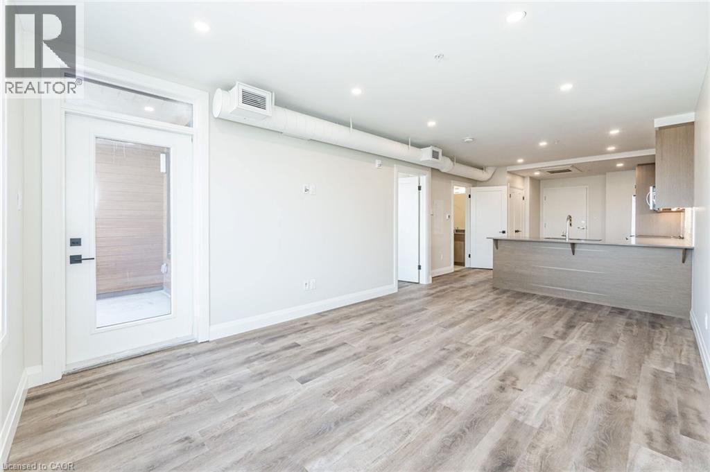 Expansive open-concept living area featuring wood-finish flooring, recessed lighting, a modern kitchen island with an undermount sink, contemporary cabinetry, and a glass-paneled exterior door - 72 Erb Street E Unit# 102, Waterloo, ON - Indoor Photo Showing Other Room