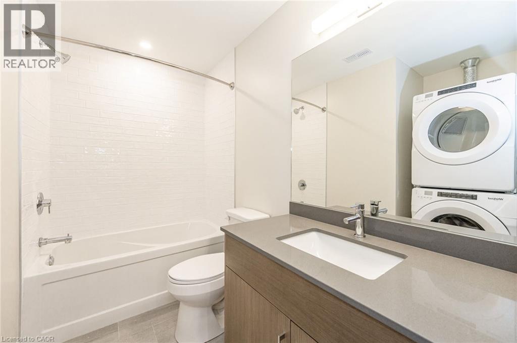 Bathroom featuring a tub/shower combination with white subway tile surround, a built-in vanity with a light gray countertop, and a stacked washer and dryer - 72 Erb Street E Unit# 102, Waterloo, ON - Indoor Photo Showing Laundry Room