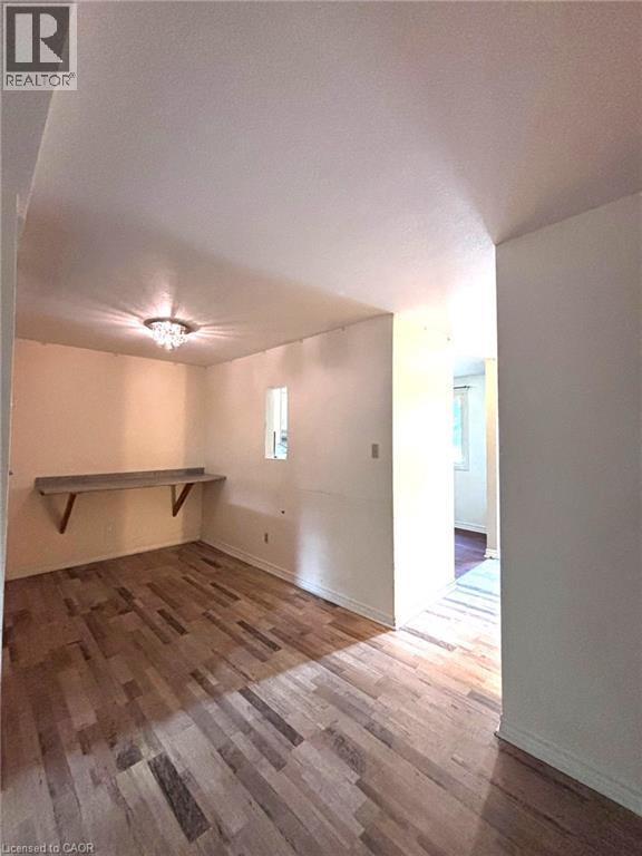 Room featuring wood-finish flooring, a built-in wall-mounted shelf, and a ceiling-mounted light fixture - 490 Third Street Unit# 40, London, ON - Indoor Photo Showing Other Room