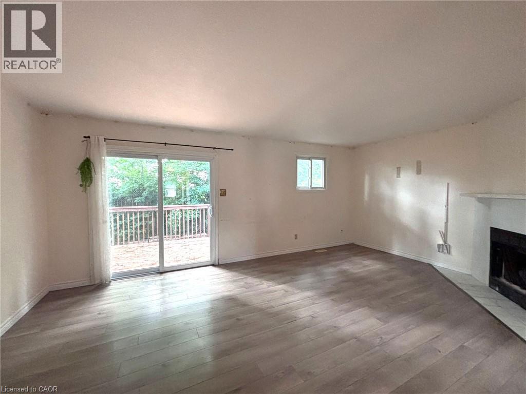 Spacious interior featuring wood-finish flooring, a fireplace with a tiled hearth, and sliding glass doors opening to an outdoor deck - 490 Third Street Unit# 40, London, ON - Indoor With Fireplace