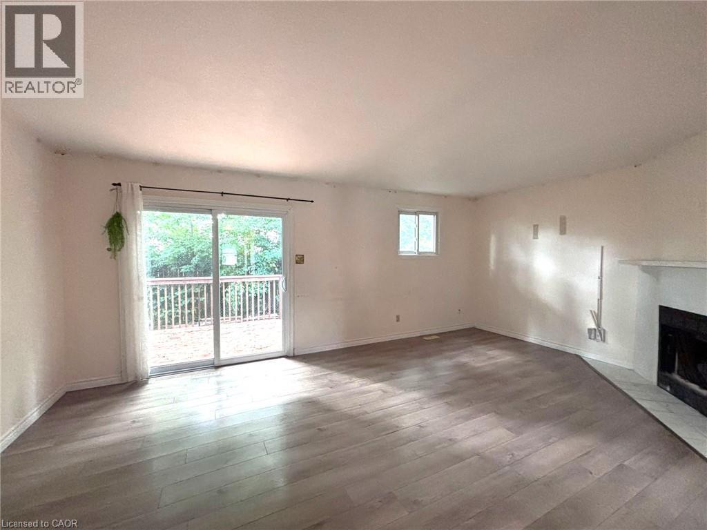 Spacious living area featuring wood-finish flooring, a white-painted fireplace with a tile hearth, and a large sliding glass door opening onto a wooden deck - 490 Third Street Unit# 40, London, ON - Indoor With Fireplace
