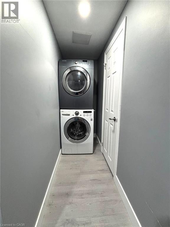 Dedicated laundry area featuring a stacked washer and dryer, wood-finish flooring, recessed lighting, and a paneled interior door - 490 Third Street Unit# 40, London, ON - Indoor Photo Showing Laundry Room