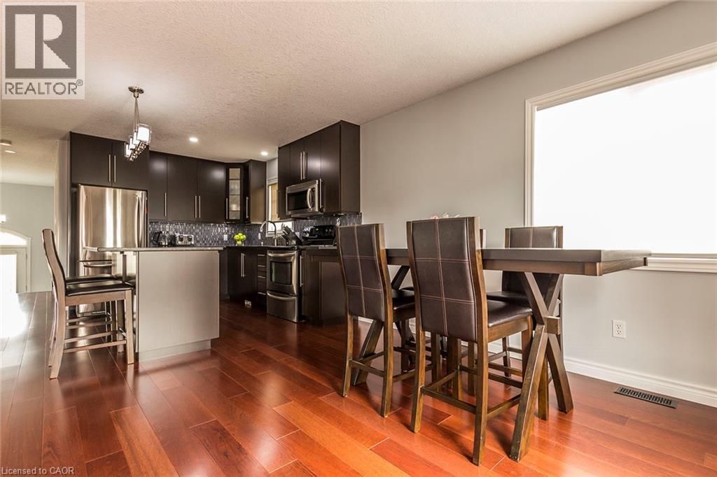 Modern kitchen featuring dark wood-finish cabinetry, stainless steel appliances, a mosaic tile backsplash, and a central island with an integrated breakfast bar - 44 Lemon Grass Street, Kitchener, ON - Indoor