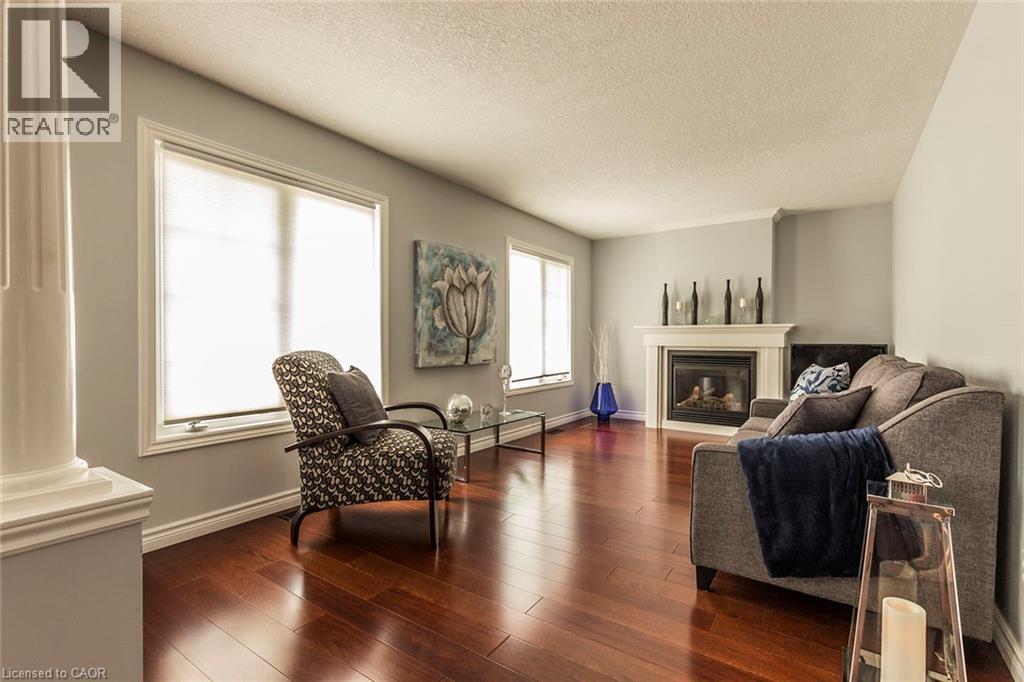 Living area featuring rich wood-finish flooring, a white mantel fireplace, and multiple windows with white trim - 44 Lemon Grass Street, Kitchener, ON - Indoor Photo Showing Living Room With Fireplace