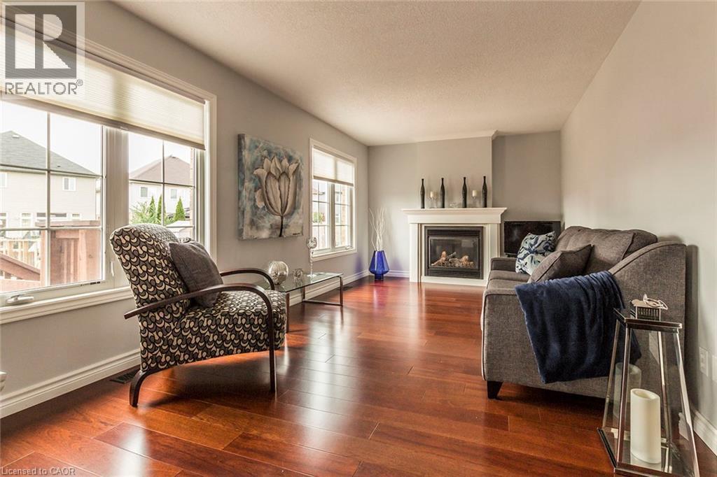 Living area featuring rich wood-finish flooring, light gray wall tones, a corner fireplace with a white mantel, and multiple windows - 44 Lemon Grass Street, Kitchener, ON - Indoor Photo Showing Living Room With Fireplace