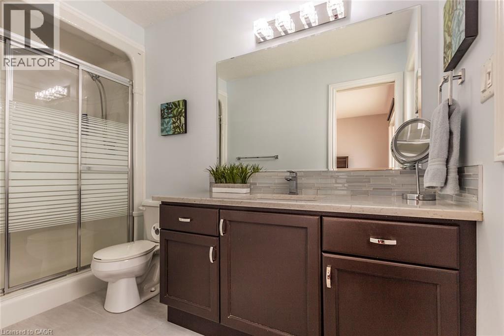 Full bathroom featuring a dark wood-finish vanity with a light-toned countertop, a glass tile backsplash, and a large wall-mounted mirror - 44 Lemon Grass Street, Kitchener, ON - Indoor Photo Showing Bathroom