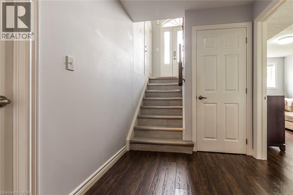 Entry foyer featuring dark wood-finish flooring, a staircase with neutral-toned treads, white trim, and a paneled door with dark hardware - 44 Lemon Grass Street, Kitchener, ON - Indoor Photo Showing Other Room