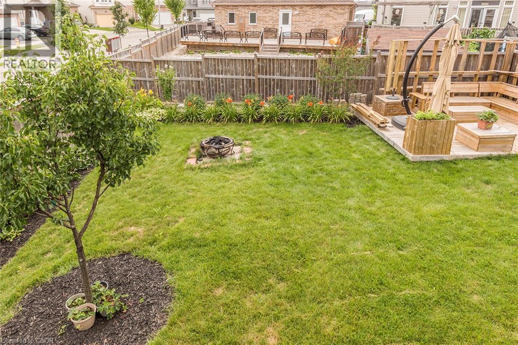 Expansive backyard featuring a lush lawn, established tree, and a built-in fire pit on a stone base - 44 Lemon Grass Street, Kitchener, ON - Outdoor