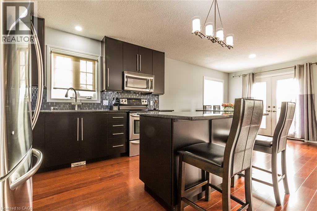 Kitchen featuring dark wood-finish cabinetry, stainless steel appliances, a tile backsplash, and a breakfast bar with seating - 44 Lemon Grass Street, Kitchener, ON - Indoor