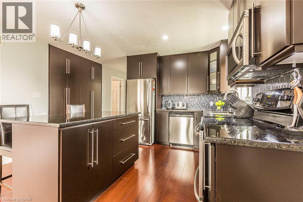 Modern kitchen featuring dark wood-finish cabinetry, stainless steel appliances, a center island with bar seating, and a mosaic tile backsplash - 44 Lemon Grass Street, Kitchener, ON - Indoor Photo Showing Kitchen With Stainless Steel Kitchen With Upgraded Kitchen