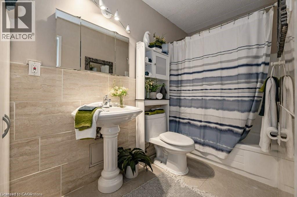 Bathroom featuring a pedestal sink, a three-door mirrored medicine cabinet, and a tiled shower/tub combination - 75 Hazelglen Drive Unit# 308, Kitchener, ON - Indoor Photo Showing Bathroom