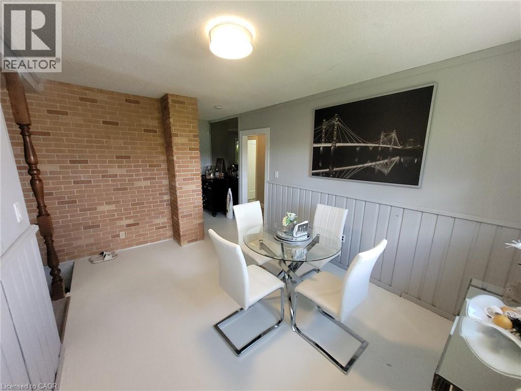 Dining area featuring light-colored flooring and a textured brick accent wall - 879 West 5Th Street, Hamilton, ON - Indoor Photo Showing Dining Room