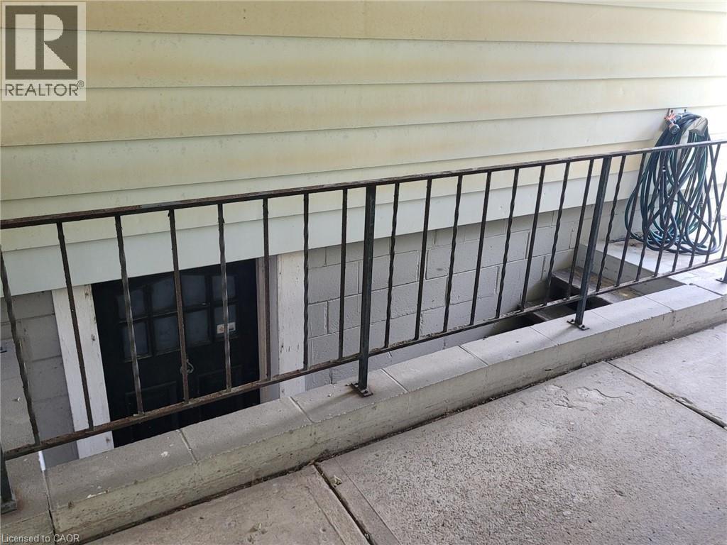 Exterior lower-level entry featuring a security door, concrete block foundation, and an exterior metal railing - 879 West 5Th Street, Hamilton, ON - Outdoor With Exterior