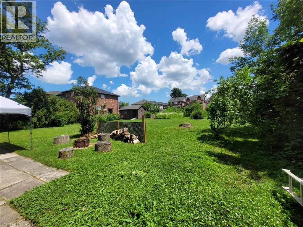 Expansive green lawn with mature trees and a dedicated fire pit area featuring log seating - 879 West 5Th Street, Hamilton, ON - Outdoor