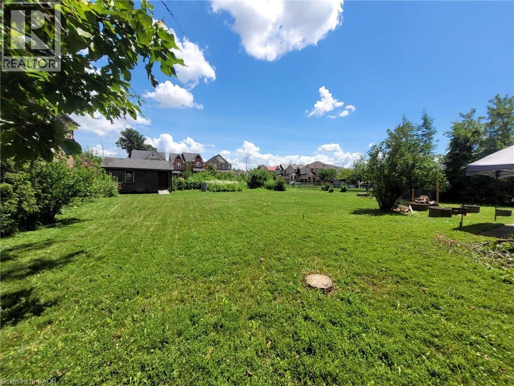 Expansive green space featuring a large lawn area, mature perimeter foliage, and a detached outbuilding - 879 West 5Th Street, Hamilton, ON - Outdoor