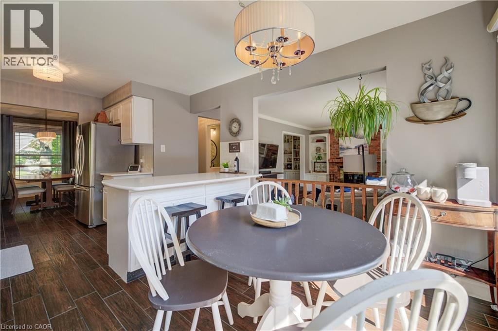 Open-concept dining area featuring wood-finish flooring, a contemporary chandelier, a breakfast bar with seating, stainless steel appliances, and a defined dining space with window views - 41 Mcniven Road, Ancaster, ON - Indoor Photo Showing Dining Room