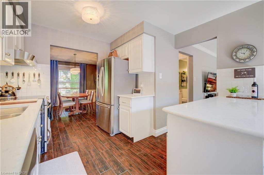 Kitchen featuring wood-finish flooring, white cabinetry, stainless steel appliances, white subway tile backsplash, and a breakfast bar with a solid surface countertop - 41 Mcniven Road, Ancaster, ON - Indoor Photo Showing Kitchen With Double Sink