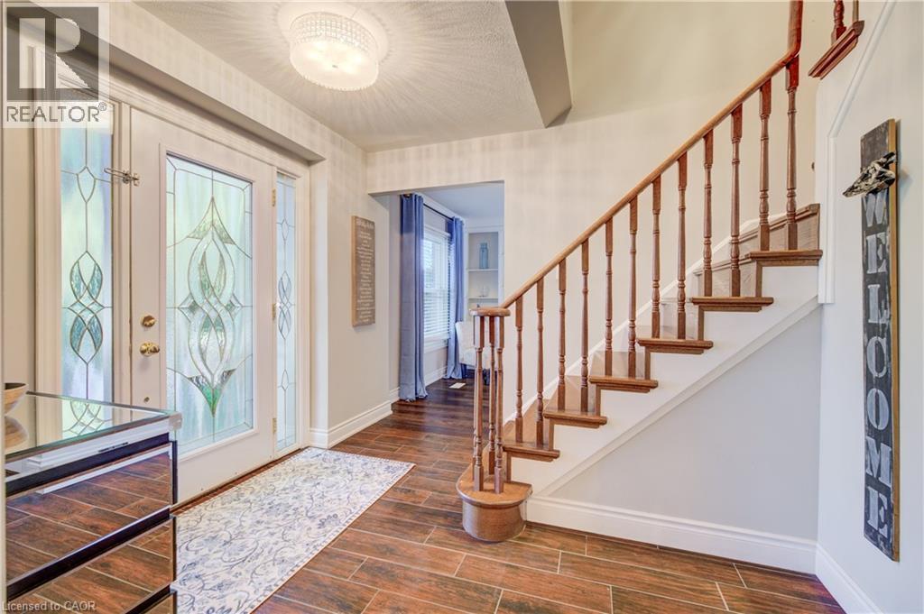 Entryway featuring a decorative glass front door with sidelights, wood-finish flooring, a traditional wooden staircase with balusters, and a contemporary flush mount light fixture - 41 Mcniven Road, Ancaster, ON - Indoor Photo Showing Other Room
