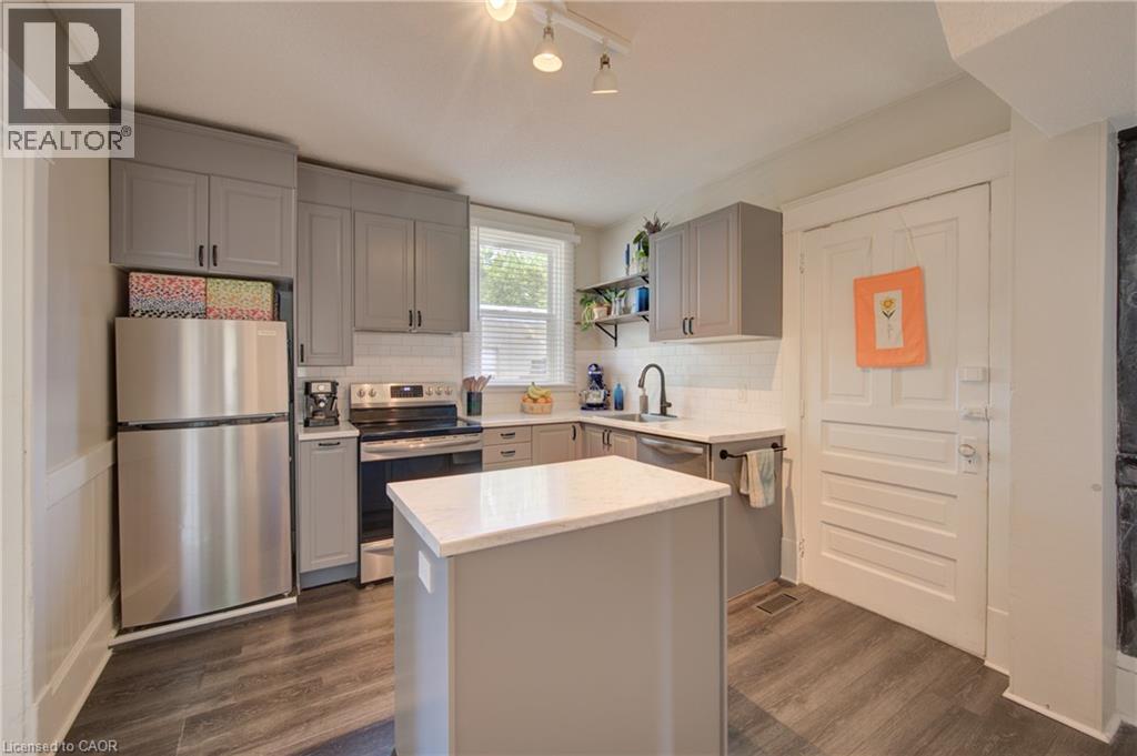 Kitchen featuring an island with a light-toned countertop, gray cabinetry, stainless steel appliances, and wood-finish flooring - 39 Kerr Street, Cambridge, ON - Indoor Photo Showing Kitchen