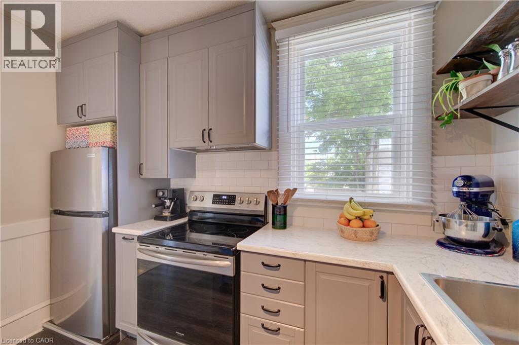 Kitchen featuring light gray cabinetry with black hardware, white subway tile backsplash, light-toned countertops, and a window with white blinds - 39 Kerr Street, Cambridge, ON - Indoor Photo Showing Kitchen