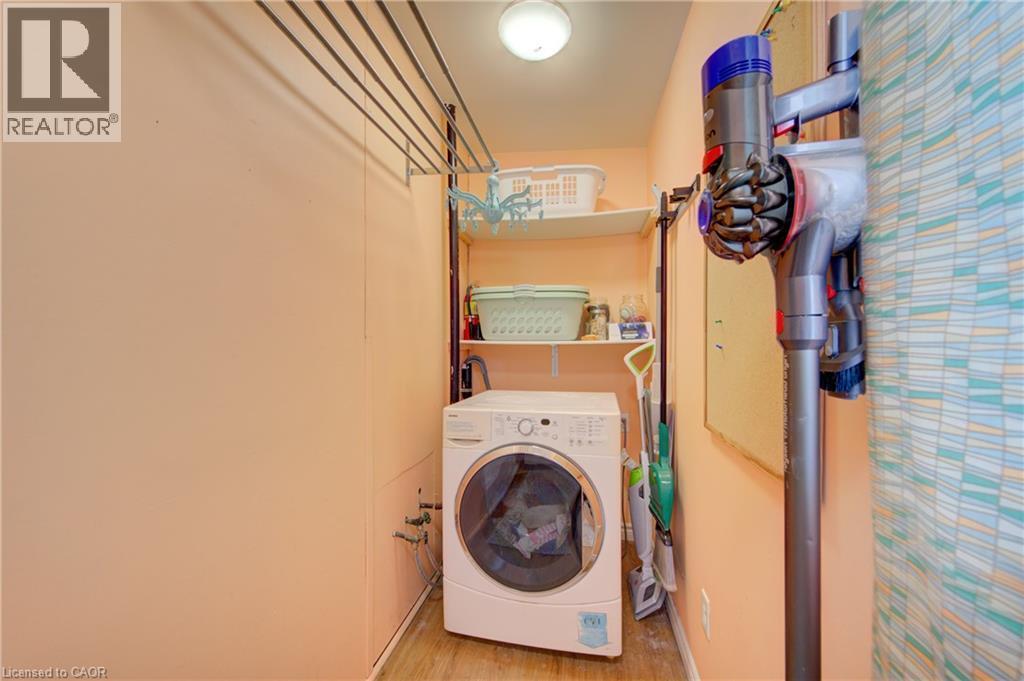 Dedicated laundry area featuring a front-load washing machine, wood-finish flooring, built-in shelving, and overhead lighting - 39 Kerr Street, Cambridge, ON - Indoor Photo Showing Laundry Room