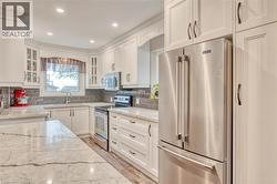 Bright kitchen featuring white cabinetry, stone countertops, a tile backsplash, stainless steel appliances, and recessed lighting -