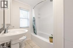 Bathroom featuring a white pedestal sink with chrome faucet, a white bathtub with a tiled surround, and a window with horizontal blinds -