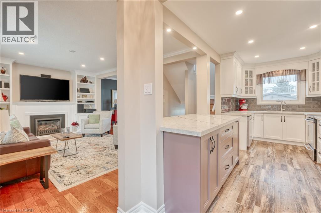 Open-concept kitchen and living area featuring a central island with a light-toned countertop, white cabinetry with glass-front accents, and a grey subway tile backsplash - 851 Beach Boulevard, Hamilton, ON - Indoor With Fireplace