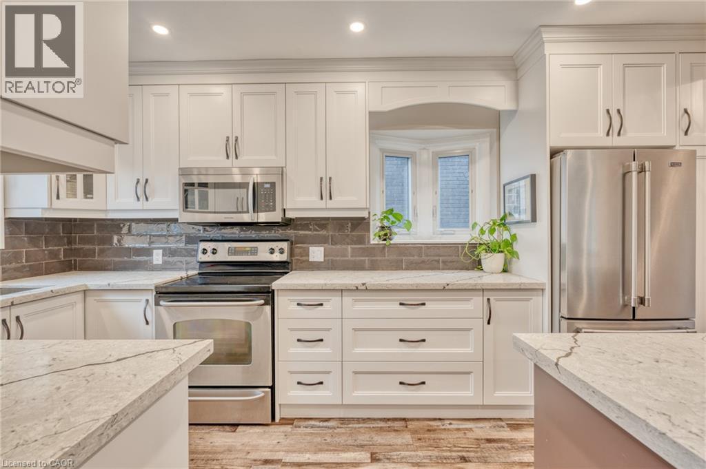 Kitchen featuring white shaker cabinetry, light-toned countertops, stainless steel appliances, and wood-finish flooring - 851 Beach Boulevard, Hamilton, ON - Indoor Photo Showing Kitchen