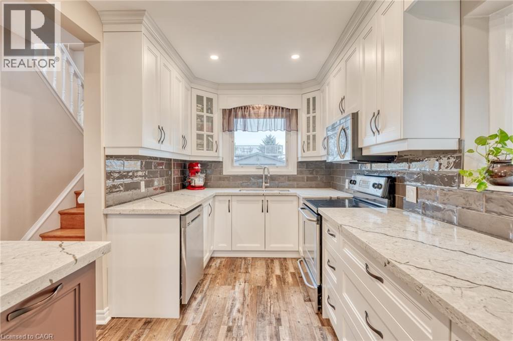 U-shaped kitchen featuring white cabinetry, light-toned countertops, and a dark tile backsplash - 851 Beach Boulevard, Hamilton, ON - Indoor Photo Showing Kitchen With Double Sink