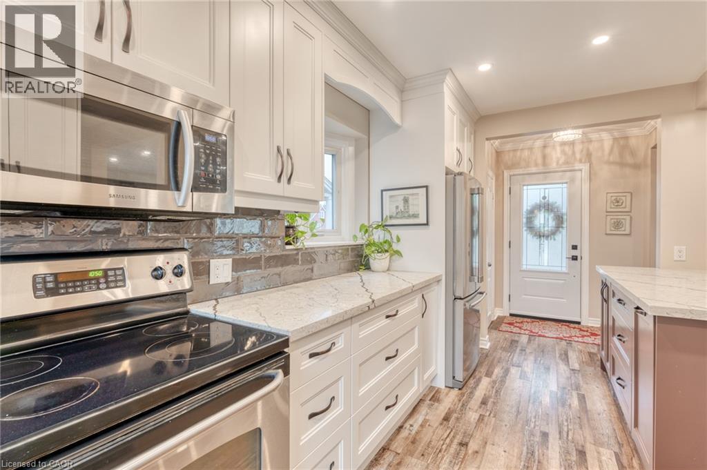 Contemporary kitchen featuring white shaker cabinetry, stainless steel appliances, a dark brick-patterned backsplash, light-toned countertops, and wood-finish flooring - 851 Beach Boulevard, Hamilton, ON - Indoor Photo Showing Kitchen With Upgraded Kitchen