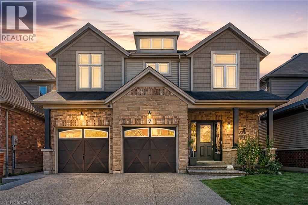 Two-story residential exterior featuring a stone and brick facade, double garage with arched windows, prominent front porch with pillars, and gabled rooflines - 7 Kinsman Drive, Binbrook, ON - Outdoor