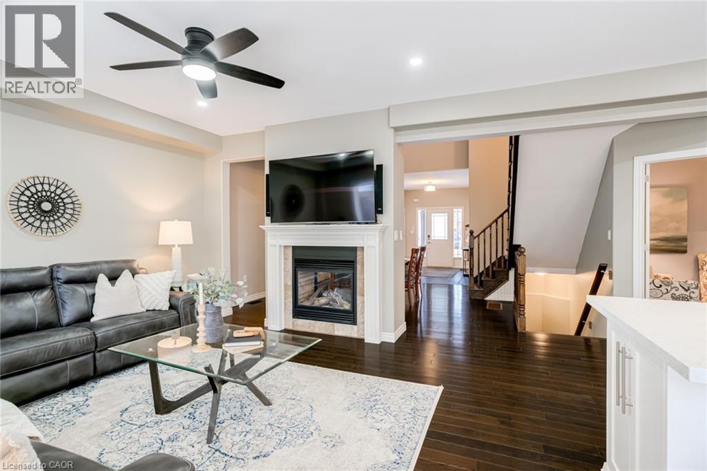 Living area featuring wood-finish flooring, a fireplace with a decorative mantel, and an overhead ceiling fan with integrated lighting - 7 Kinsman Drive, Binbrook, ON - Indoor Photo Showing Living Room With Fireplace