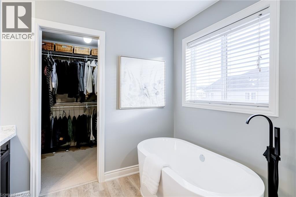 Freestanding soaking tub with a matte black floor-mounted faucet, complemented by light wood-finish flooring - 7 Kinsman Drive, Binbrook, ON - Indoor Photo Showing Bathroom