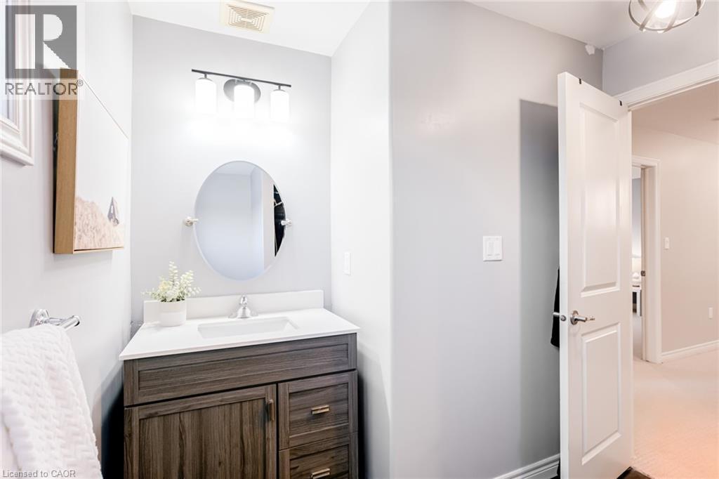 Powder room featuring a wood-finish vanity with drawer and cabinet storage, a white countertop with an integrated sink, and an oval mirror - 7 Kinsman Drive, Binbrook, ON - Indoor Photo Showing Bathroom