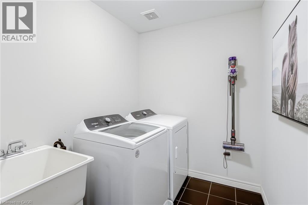 Dedicated laundry area featuring a utility sink with dual-handle faucet, top-load washing machine, front-load dryer, and dark square tile flooring - 7 Kinsman Drive, Binbrook, ON - Indoor Photo Showing Laundry Room