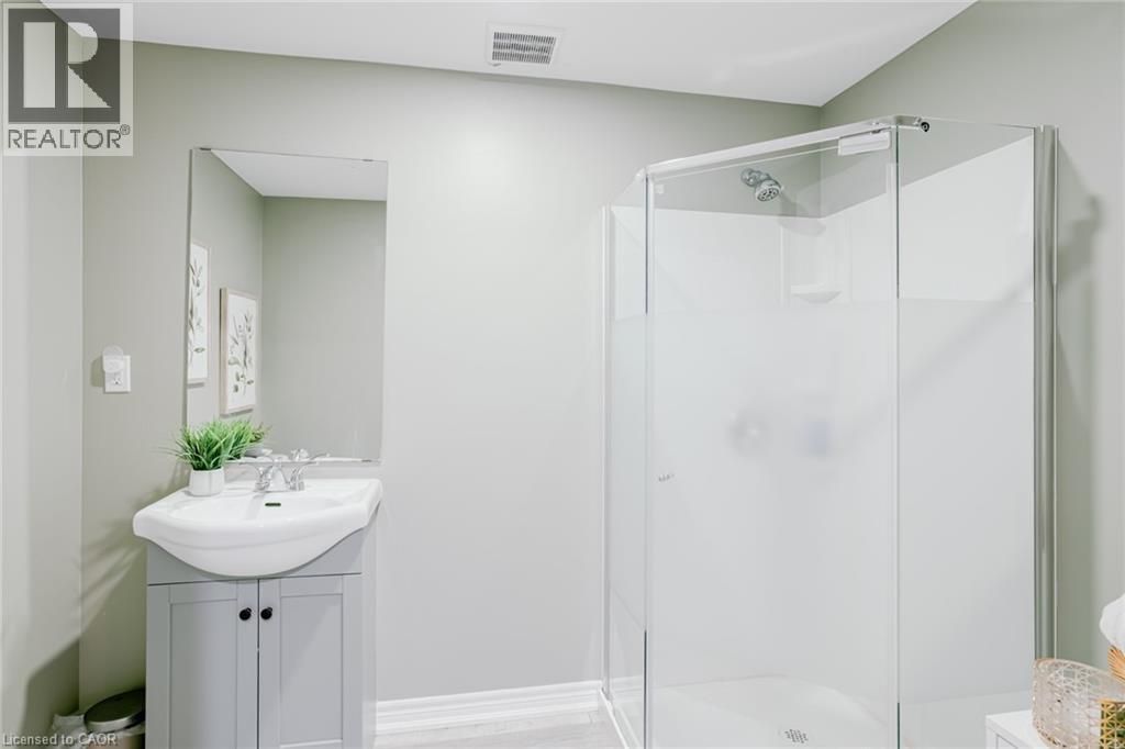 Bathroom featuring a glass-enclosed shower, a vanity with a white ceramic sink, a rectangular wall-mounted mirror, and light-toned walls - 7 Kinsman Drive, Binbrook, ON - Indoor Photo Showing Bathroom
