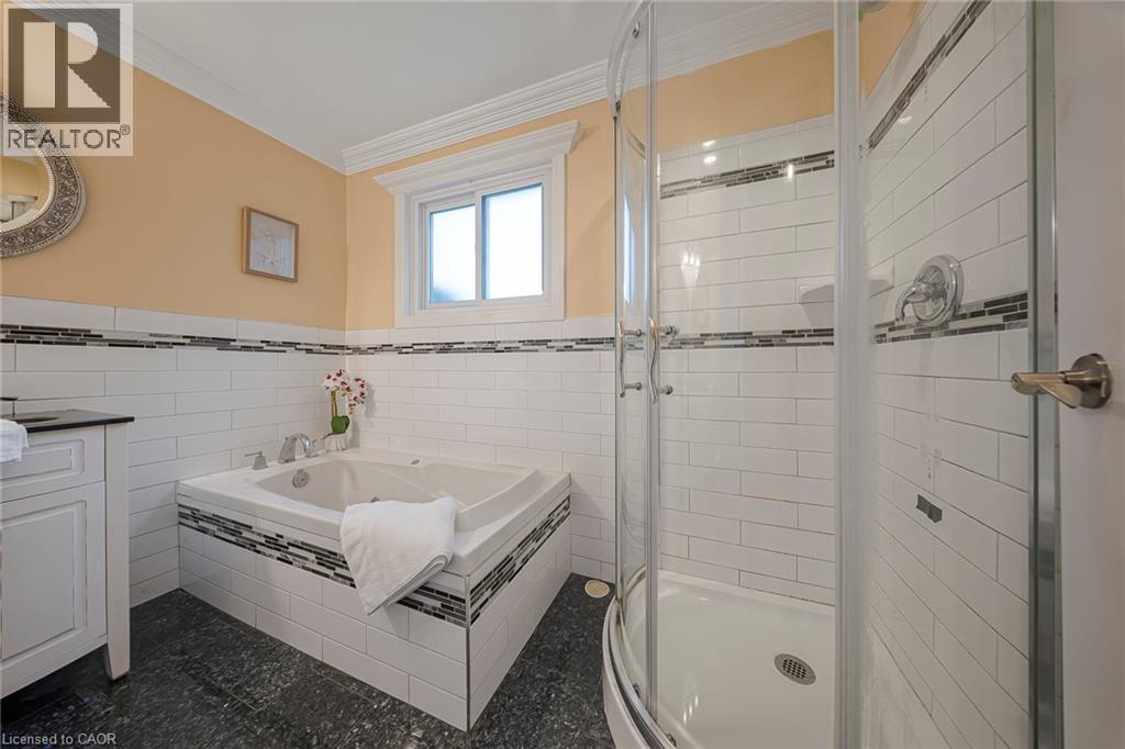 Bathroom featuring a corner soaking tub with mosaic tile accents, a separate glass-enclosed shower, subway tile surround, and dark-finish flooring - 124 Dunsmere Drive, Kitchener, ON - Indoor Photo Showing Bathroom