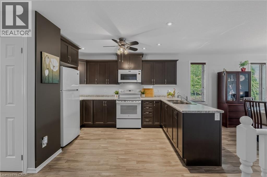 Kitchen featuring dark wood-finish cabinetry, light-toned countertops, and a white subway tile backsplash - 51 Millcroft Drive, Simcoe, ON - Indoor Photo Showing Kitchen With Double Sink