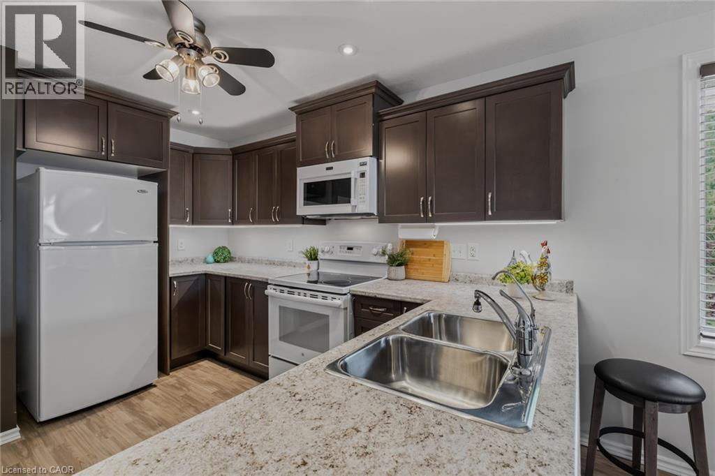Kitchen featuring dark wood-finish cabinetry, light speckled countertops, and a white tile backsplash - 51 Millcroft Drive, Simcoe, ON - Indoor Photo Showing Kitchen With Double Sink