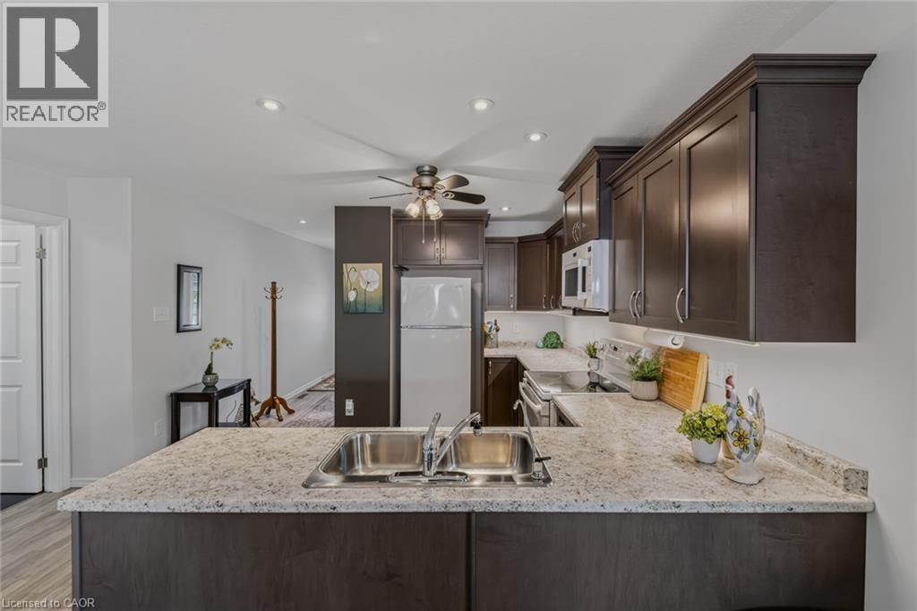 Kitchen featuring an integrated stainless steel double basin sink, dark wood-finish cabinetry, light speckled countertops, and a white appliance suite - 51 Millcroft Drive, Simcoe, ON - Indoor Photo Showing Kitchen With Double Sink