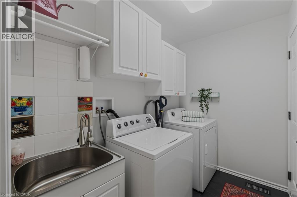 Dedicated laundry space featuring white cabinetry, a utility sink with a pull-down faucet, and white tile backsplash - 51 Millcroft Drive, Simcoe, ON - Indoor Photo Showing Laundry Room