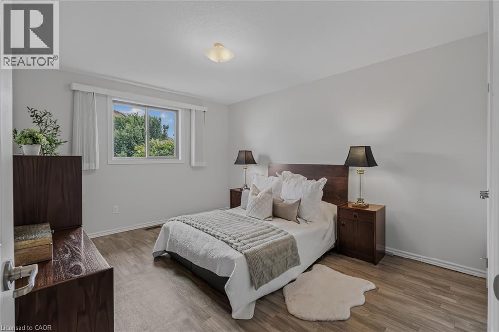 Spacious bedroom featuring light neutral wall paint, wood-finish flooring, a white window frame, and a flush mount ceiling light fixture - 51 Millcroft Drive, Simcoe, ON - Indoor Photo Showing Bedroom