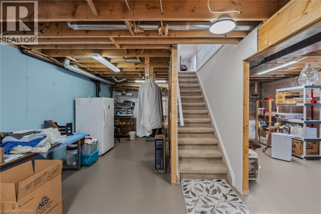 Unfinished basement space featuring exposed wood joists and structural beams, a carpeted staircase with white railings, and painted foundation walls - 51 Millcroft Drive, Simcoe, ON - Indoor Photo Showing Basement