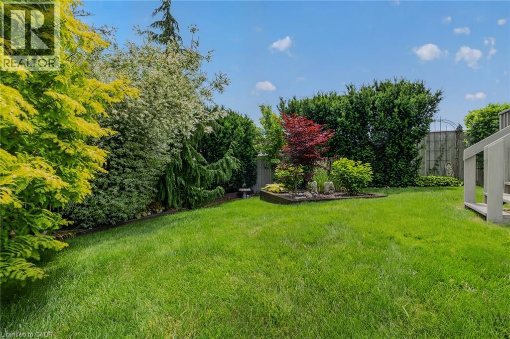 Expansive lawn featuring mature trees and shrubs, a raised garden bed, and a partial deck structure - 51 Millcroft Drive, Simcoe, ON - Outdoor
