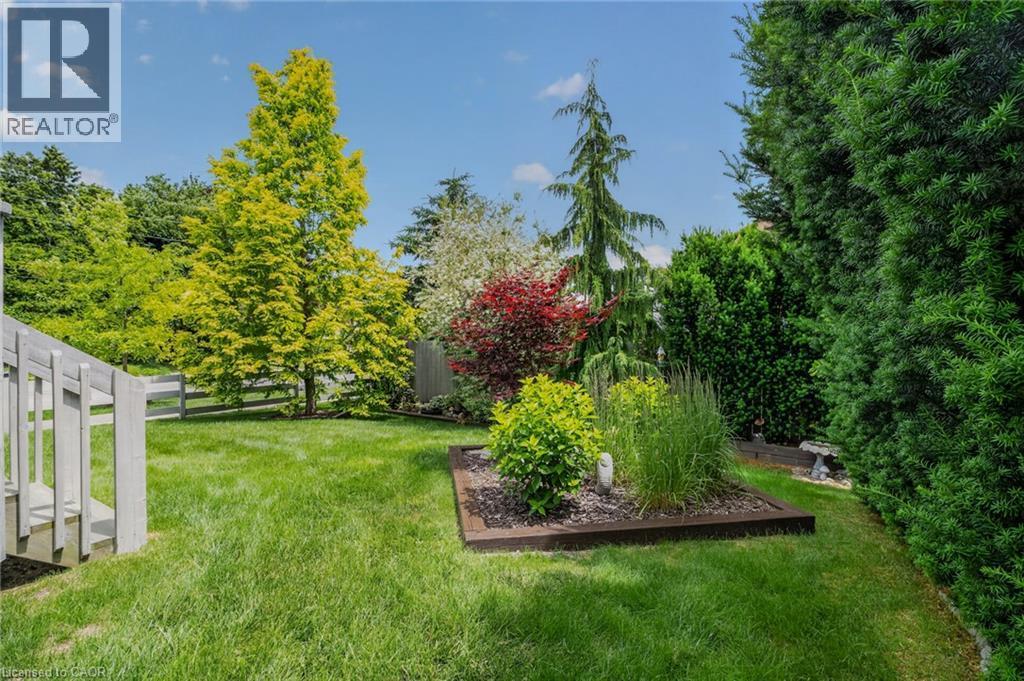 Expansive lawn area featuring a raised garden bed with established plantings, mature trees, a privacy hedge, and a partial wood fence - 51 Millcroft Drive, Simcoe, ON - Outdoor