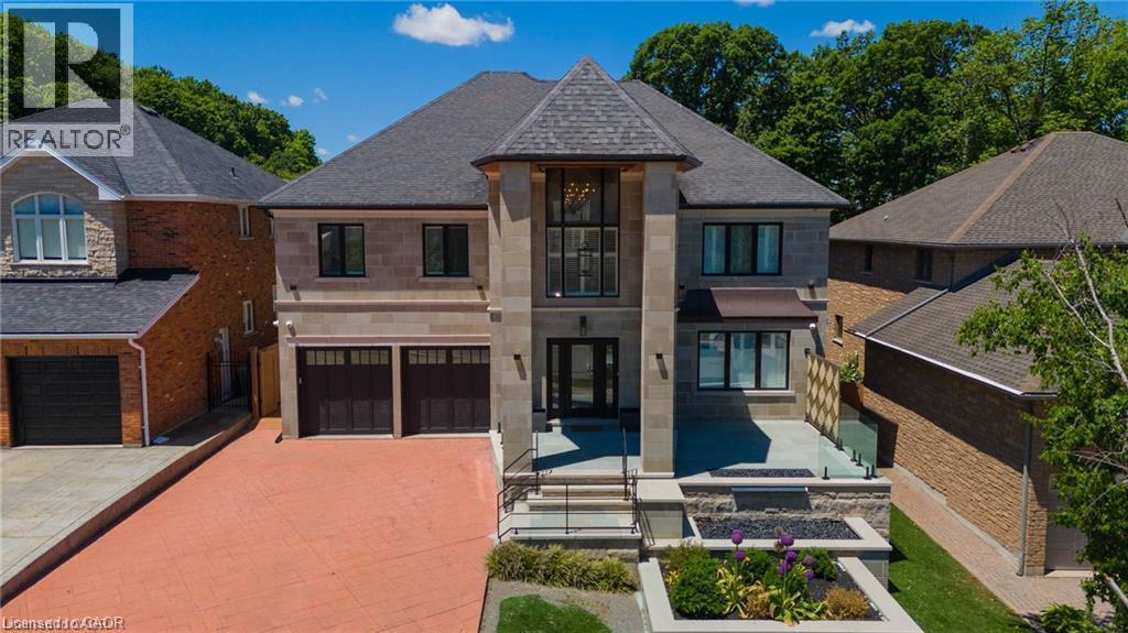 Stone and stucco exterior featuring a grand entrance with a full-height window, a peaked roofline, an integrated two-car garage, a glass-paneled balcony, and a red-toned driveway - 76 Adriatic Boulevard, Hamilton, ON - Outdoor
