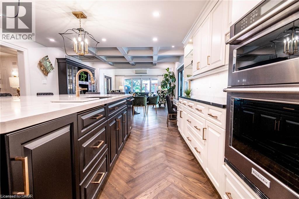 Gourmet kitchen featuring a large island with sink, white countertops, built-in double ovens, white and dark cabinetry, and herringbone wood-finish flooring - 76 Adriatic Boulevard, Hamilton, ON - Indoor Photo Showing Kitchen